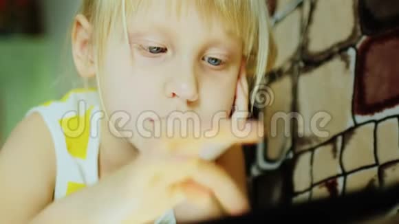一个小女孩在平板电脑上玩躺在沙发上手指按在屏幕上视频的预览图