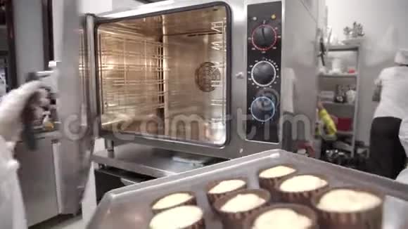 厨师把烤盘和纸杯蛋糕放进烤箱烤盘上的生饼视频的预览图