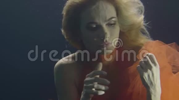 一位身着橙色礼服的金发女子在黑暗背景下潜泳视频的预览图