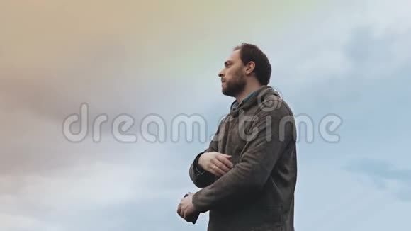 留着胡子的欧洲男人拿着智能手机站着低角度惊人的天空景观休闲帅哥拍智能手机照4公里视频的预览图