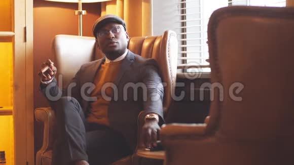 美国黑人男子戴着黑帽子坐在椅子上抽着雪茄视频的预览图