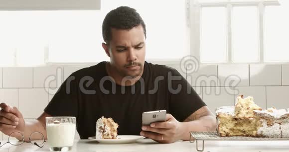 带着智能手机的黑人混血男子早餐吃蛋糕和牛奶视频的预览图