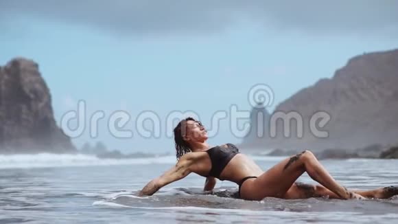女人在靠近大海的沙滩上在群山和黑沙上翩翩起舞视频的预览图