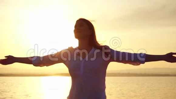 女人在湖边日落时举起手臂女性在黄金时刻缓慢地伸出双手视频的预览图