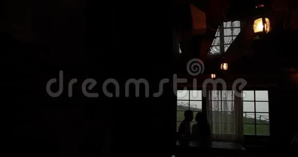 一对接吻情侣坐在山上某处黑房子的窗户前的剪影视频的预览图