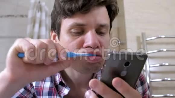 年轻人刷牙在浴室里看电话视频的预览图