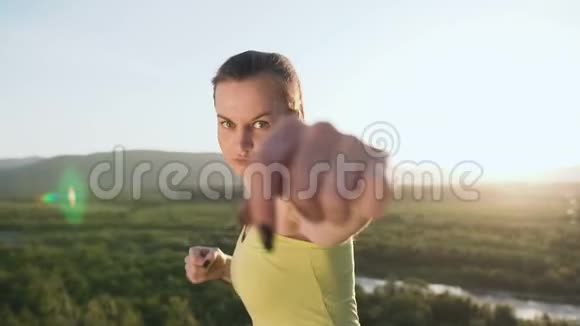 快关门美丽的踢拳女孩训练在山顶日落或日出在夏天愤怒的年轻女子视频的预览图