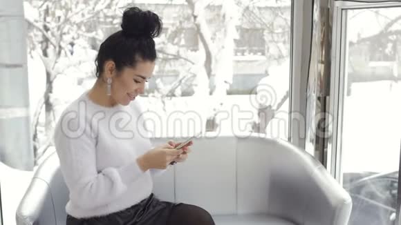美女使用智能手机坐在寡妇身边的沙发上视频的预览图