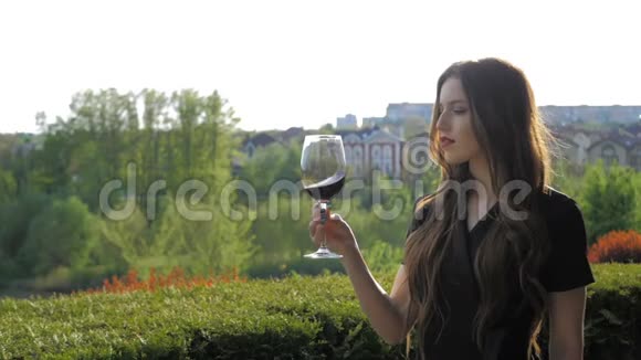 年轻性感的女孩红唇在大自然的背景上旋转着一杯红酒视频的预览图