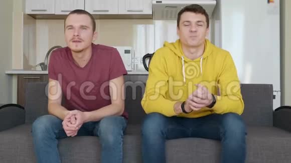 两个人坐在沙发上看电视上的足球比赛享受他们最喜欢的球队的胜利视频的预览图