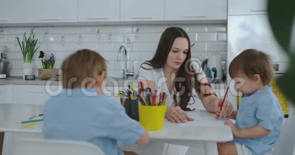 妈妈帮儿子学画做作业学前准备在家坐在白色厨房两个兄弟视频的预览图