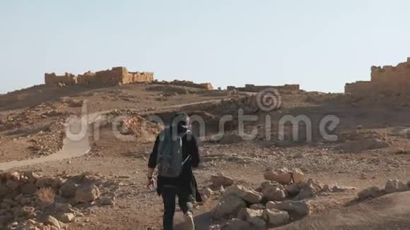 带背包的人在古老的废墟中徒步旅行放松的欧洲男性旅行者走在沙漠岩石和沙子上以色列4K视频的预览图