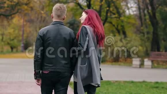 巴克尔观赏浪漫的年轻夫妇在秋天公园散步的白天年轻的金发男子皮革后景视频的预览图