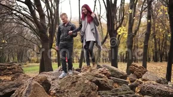 浪漫的年轻夫妇在秋天公园的岩石上散步白天牵手关心他的男朋友在哭视频的预览图