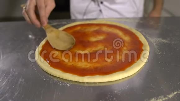 厨师手正在将巴氏杀菌番茄酱铺在披萨基地的特写上视频的预览图