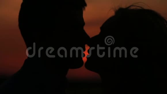 这对迷人的剪影夫妇在夕阳红的天空背景下轻轻亲吻的特写肖像视频的预览图
