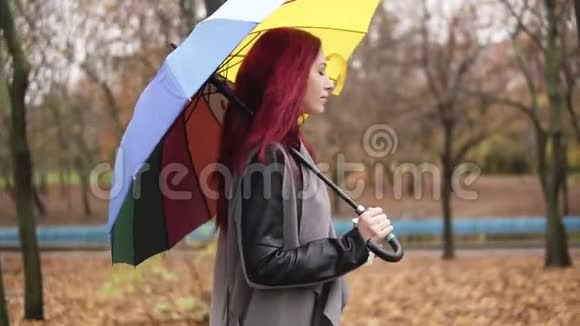 侧景一位红头发的年轻女子在秋天公园散步一边拿着五颜六色的杯子喝咖啡视频的预览图