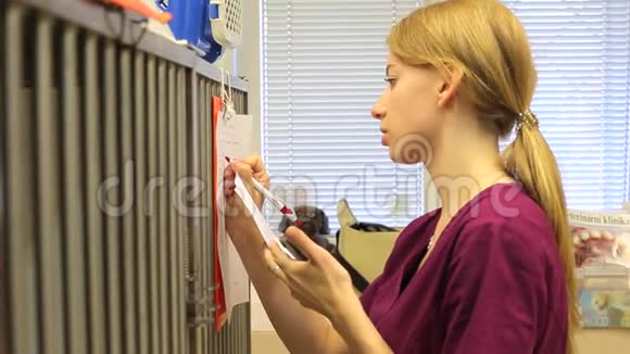 兽医诊所的一位年轻的女护士在一张贴在动物笼子上的剪贴板上写着纸视频的预览图