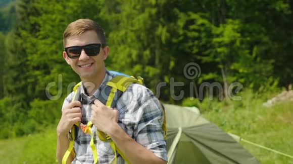 快乐的男性旅行者的肖像微笑着看着摄像机站在帐篷附近露营视频的预览图