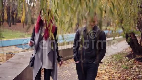 浪漫的年轻夫妇白天在秋天公园的树下散步地上的金叶毯视频的预览图