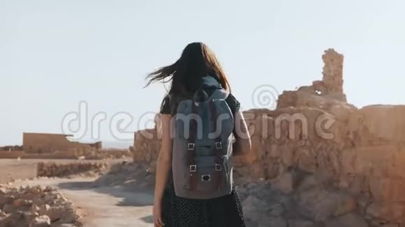 背着背包的女人走在古老的墙壁之间迷人的白种人女游客欣赏山景马萨达4K视频的预览图