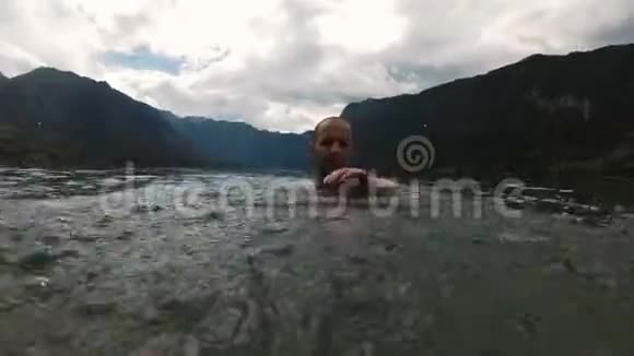 把水溅到摄像机上微笑的男孩慢动作美丽的山湖视频的预览图