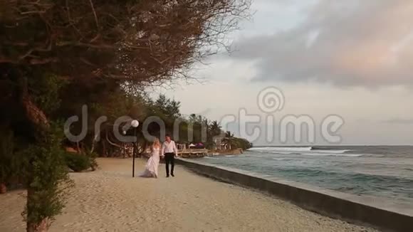 镜头跟随新娘新郎在豪华度假村桥上的平房附近沿着海岸线走向仪式视频的预览图