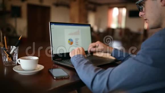 自由职业者商人戴眼镜后视图在笔记本电脑上工作并在咖啡厅屏幕上查看图表视频的预览图