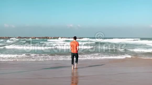 年轻人在夏天的海边从海浪中奔跑长胡子的白种人尝试冷水享受快乐的假期4K视频的预览图