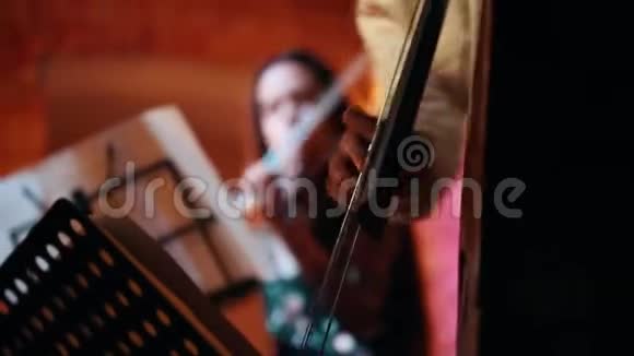 在前景中男人手演奏弦乐器在背景中女人演奏小提琴视频的预览图