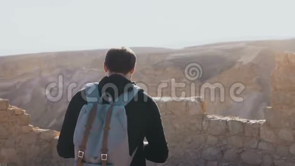 男性摄影师沿着以色列古遗址漫步去马萨达堡垒的路带背包的年轻人拍照4K视频的预览图