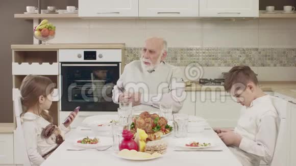 在家庭晚餐前爷爷和孙子孙女在餐桌上交流视频的预览图
