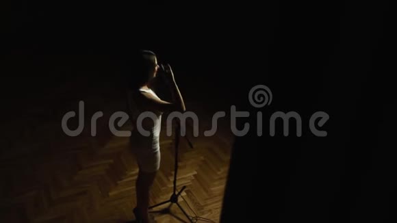 年轻女子留着长发穿着优雅的白色连衣裙带着麦克风站在舞台上视频的预览图