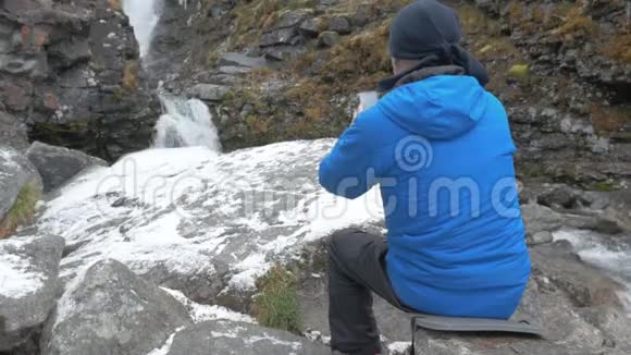 一个穿着运动服的人在瀑布附近休息3他在山上拍了一幅美丽的风景画视频的预览图