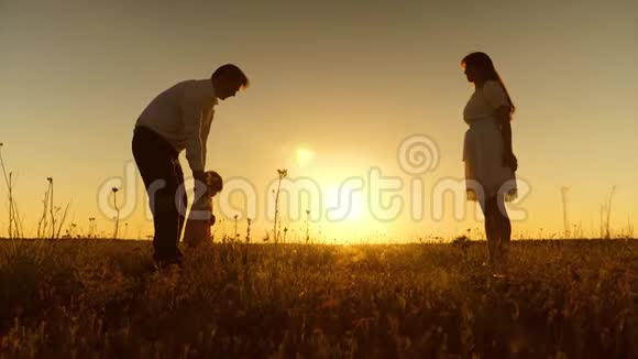 年轻的父母教孩子在金色的夕阳下用脚走路视频的预览图