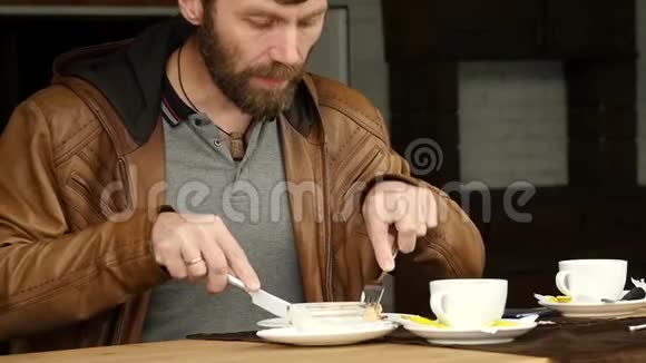 大胡子男人正在户外咖啡馆的露台上吃早餐慢动作视频的预览图