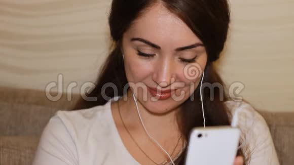 特写肖像年轻女子戴着耳机手里拿着一部手机美丽的女孩深色头发视频的预览图