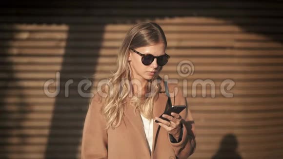 秋天一位身穿外套站着看智能手机的金发美女视频的预览图