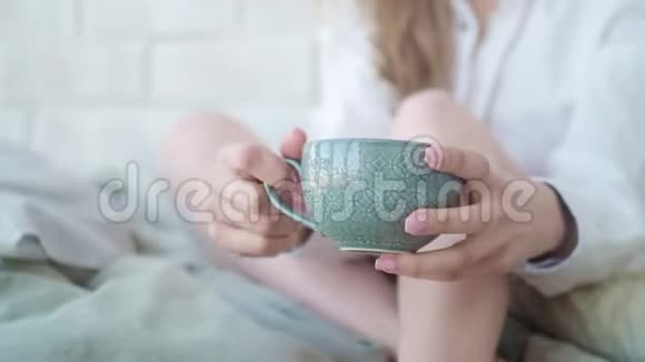 美丽的女孩坐在床上喝着茶看着相机微笑着相机在杯子后面移动视频的预览图