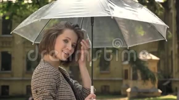 年轻漂亮的女孩白天带着伞在公园里散步夏天微笑着看着镜头视频的预览图