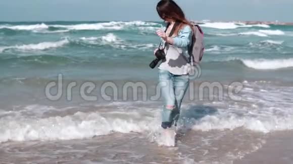 美丽的白人女孩从海滩上的波浪中奔跑漂亮的女人对着镜头微笑风吹在头发上慢动作视频的预览图