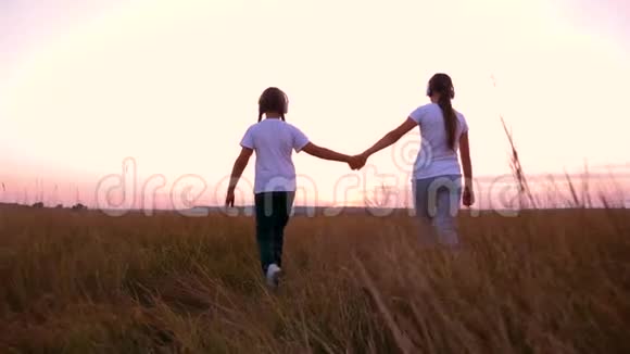 女孩牵着手在日落时走在茂密高大的草地上带着耳机听音乐的女朋友视频的预览图