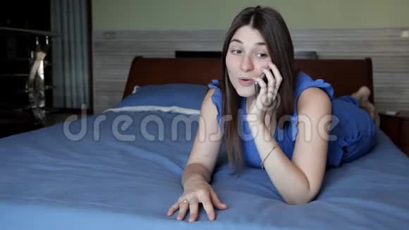 一个年轻女孩正躺在旅馆的房间里躺在一张蓝色的床上打电话视频的预览图