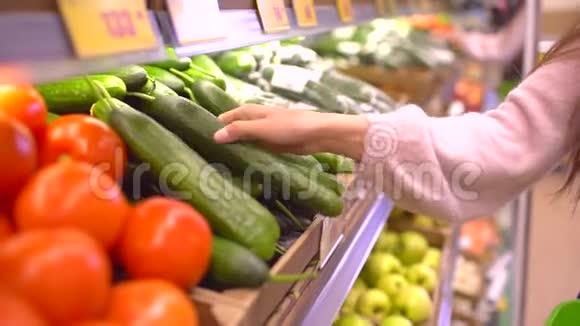 一个女人在蔬菜货架上的超市里买蔬菜和水果女人选黄瓜慢动作视频的预览图