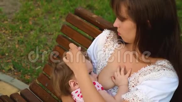 小宝宝从妈妈的乳房里吸奶妈妈正在给孩子喂奶坐在公园长椅上视频的预览图