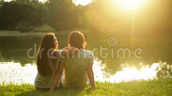 英俊的男人和漂亮的女人看着湖水和日落一对浪漫可爱的情侣的后景视频的预览图