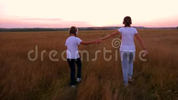 女朋友在现场用耳机听音乐女孩握着手在夕阳下茂密高大的草地上散步视频的预览图