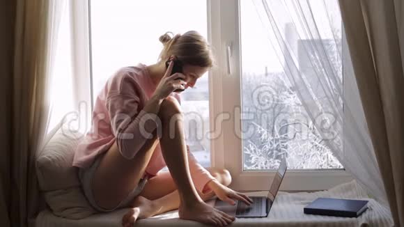 女人在她的笔记本电脑上工作在窗台上打电话视频的预览图
