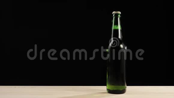 新鲜啤酒手拿一个绿色的瓶子和美味的工艺啤酒从木桌上黑色背景冷鲜啤酒视频的预览图