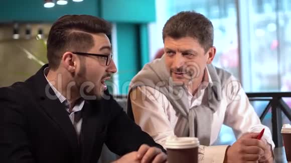 一个成熟的帅哥和一个戴眼镜的年轻人正在咖啡馆里谈话视频的预览图